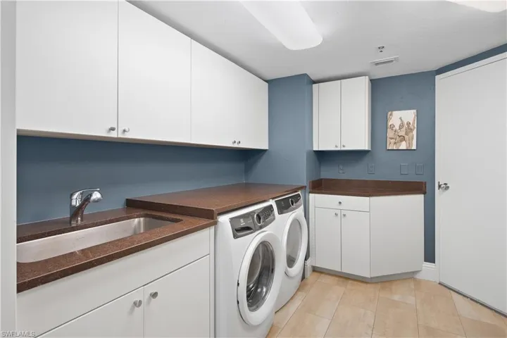 Washroom with sink, light tile flooring, cabinets, and washing machine and dryer