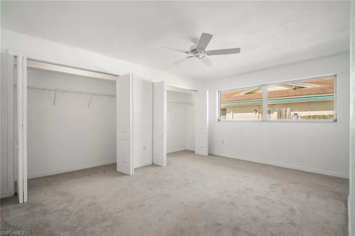 Unfurnished bedroom with carpet flooring, baseboards, ceiling fan, and multiple closets