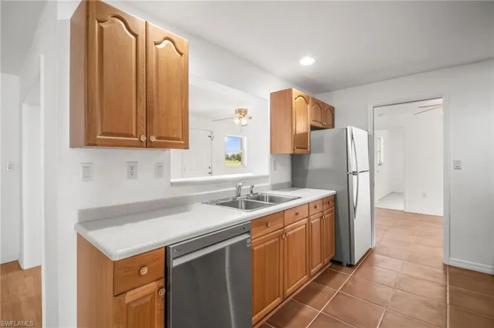 Kitchen with a sink, a ceiling fan, light countertops, dishwasher, and freestanding refrigerator