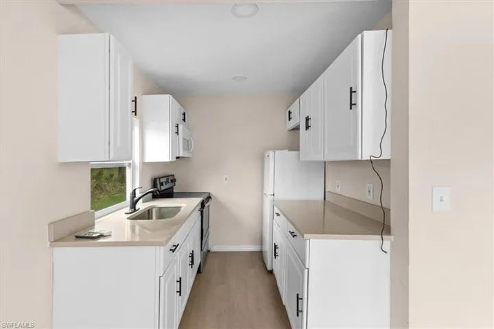 Kitchen with white cabinetry, white appliances, sink, and light hardwood / wood-style flooring
