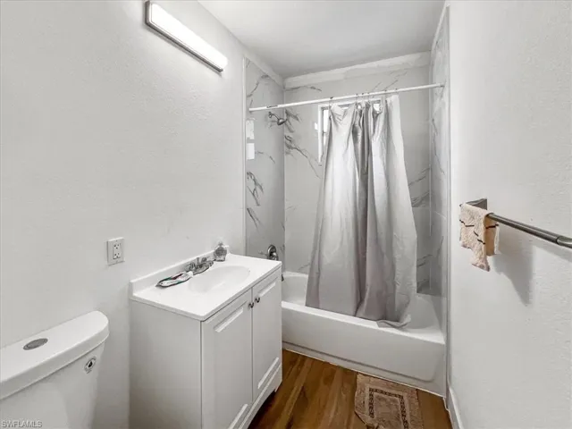 Full bathroom with wood-type flooring, vanity, shower / tub combo, and toilet