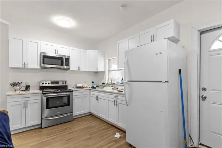 Kitchen with sink, white cabinets, stainless steel appliances, and light hardwood / wood-style floors