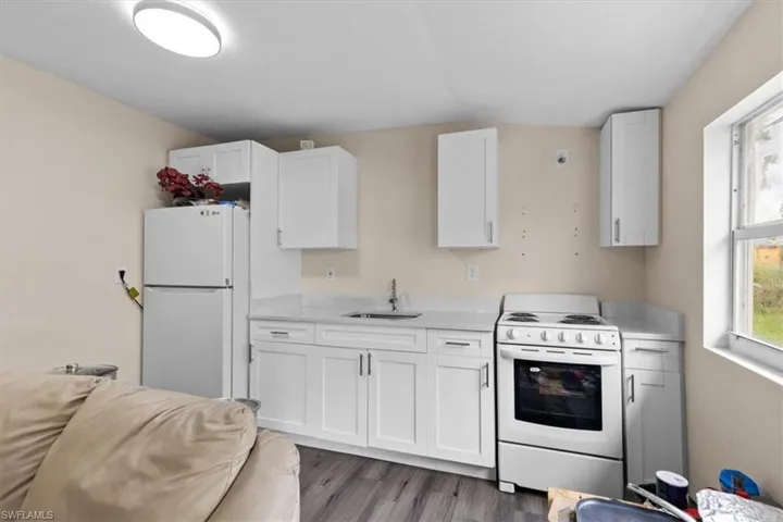 Kitchen with sink, white cabinets, white appliances, and hardwood / wood-style flooring
