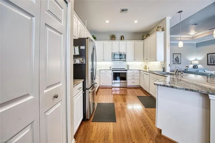 Kitchen with stainless steel appliances, light hardwood / wood-style flooring, kitchen peninsula, dark stone countertops, and hanging light fixtures