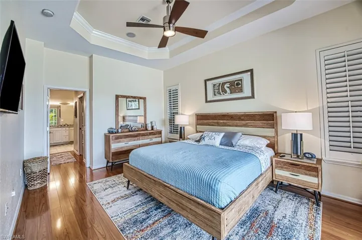 Bedroom with hardwood / wood-style floors, ensuite bathroom, a tray ceiling, ceiling fan, and crown molding