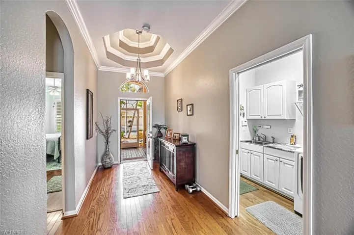 Doorway featuring light hardwood / wood-style floors, ornamental molding, an inviting chandelier, sink, and a tray ceiling