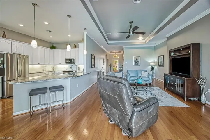 Living room featuring ceiling fan, light hardwood / wood-style flooring, a tray ceiling, and ornamental molding