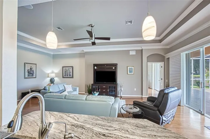 Living room featuring light hardwood / wood-style floors, ornamental molding, ceiling fan, and a tray ceiling