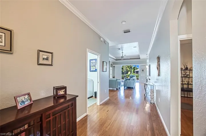 Hall featuring hardwood / wood-style flooring, a raised ceiling, and crown molding