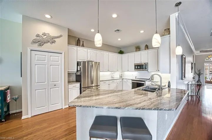 Kitchen with backsplash, sink, appliances with stainless steel finishes, hardwood / wood-style flooring, and pendant lighting