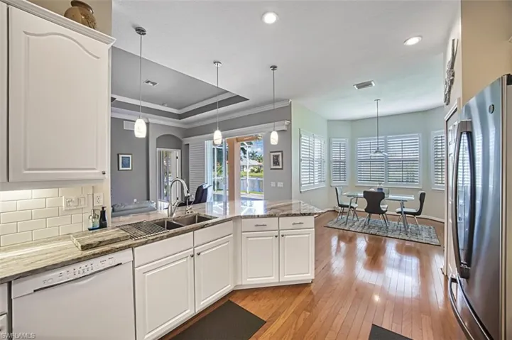 Kitchen featuring decorative light fixtures, light hardwood / wood-style floors, dishwasher, sink, and stainless steel fridge