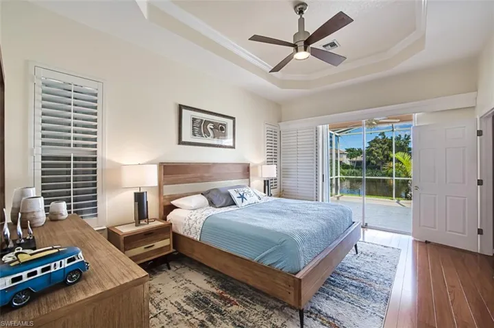 Bedroom featuring ceiling fan, light hardwood / wood-style floors, a raised ceiling, and access to outside