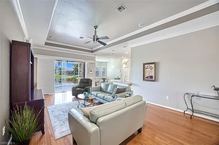 Living room with hardwood / wood-style floors, sink, a tray ceiling, ceiling fan, and crown molding