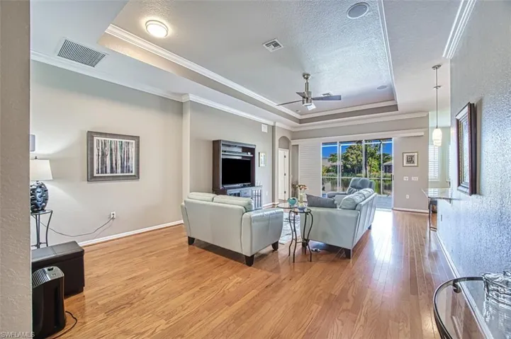 Living room with ceiling fan, hardwood / wood-style flooring, ornamental molding, and a tray ceiling