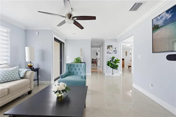 Living room featuring a ceiling fan, light tile patterned flooring, and crown molding