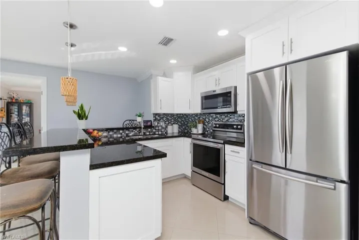 Kitchen with appliances with stainless steel finishes, backsplash, a breakfast bar area, dark stone countertops, and white cabinetry