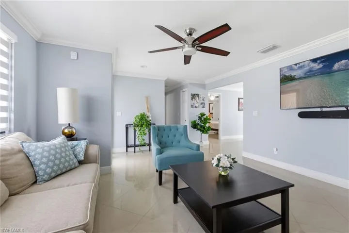 Living room featuring ceiling fan, light tile patterned flooring, and ornamental molding