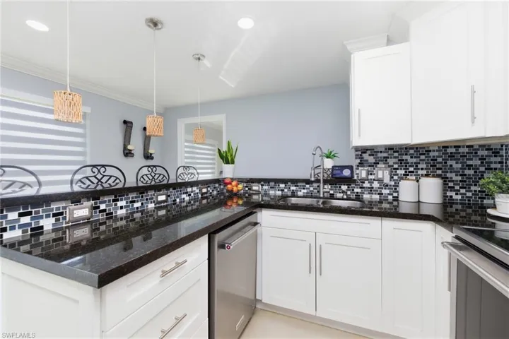 Kitchen with dark stone counters, white cabinets, hanging light fixtures, stainless steel appliances, and recessed lighting