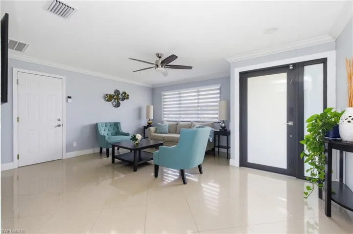 Living room with crown molding, light tile patterned flooring, and ceiling fan
