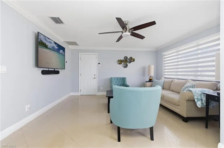 Living room with ornamental molding, light tile patterned floors, and a ceiling fan