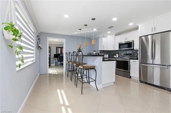 Kitchen featuring appliances with stainless steel finishes, a breakfast bar area, decorative backsplash, an office area, and decorative light fixtures