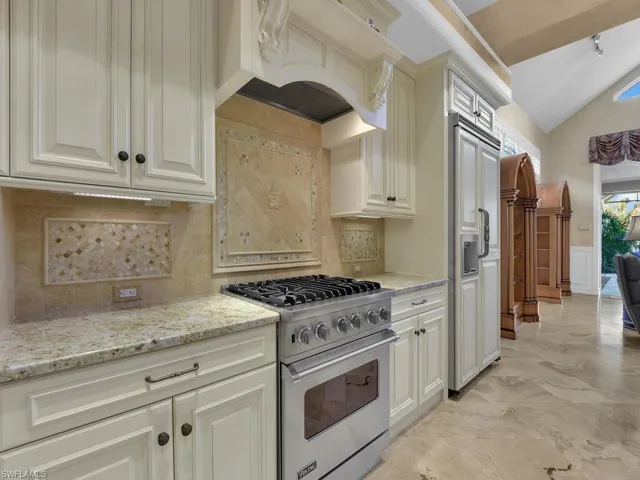 Kitchen with high end appliances, light stone counters, decorative backsplash, a wainscoted wall, and vaulted ceiling
