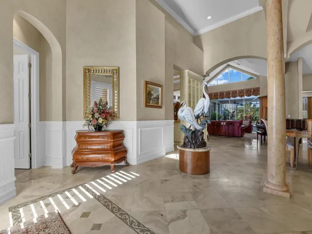 Entryway featuring arched walkways, a decorative wall, high ceiling, wainscoted wall, and decorative columns.