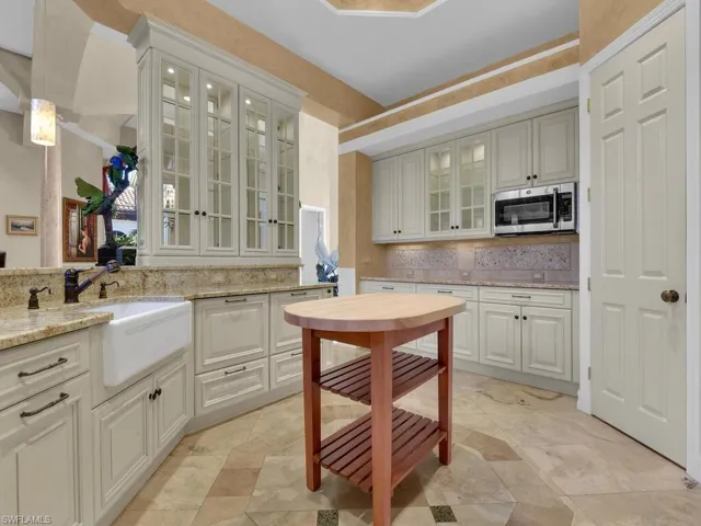Kitchen with light stone countertops, stainless steel microwave, and glass insert cabinets