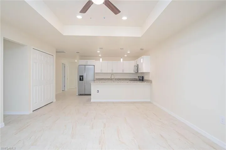 Kitchen featuring stainless steel appliances, kitchen peninsula, light stone countertops, a raised ceiling, and white cabinets