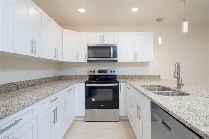 Kitchen featuring stainless steel appliances, light stone counters, sink, white cabinetry, and decorative light fixtures