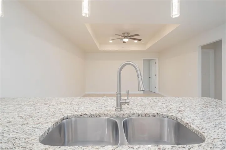 Details with light stone counters, hanging light fixtures, sink, a tray ceiling, and ceiling fan
