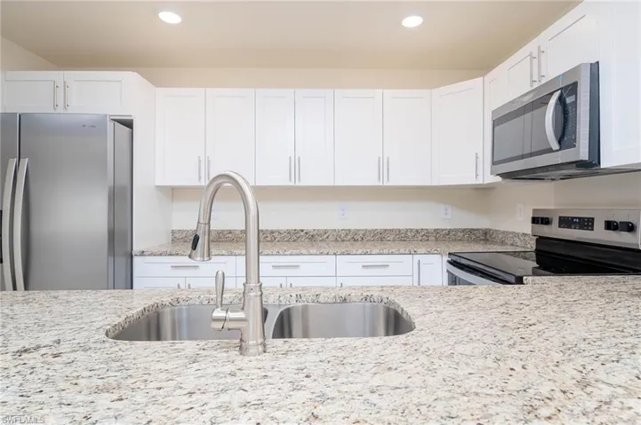 Kitchen with white cabinets, stainless steel appliances, sink, and light stone countertops