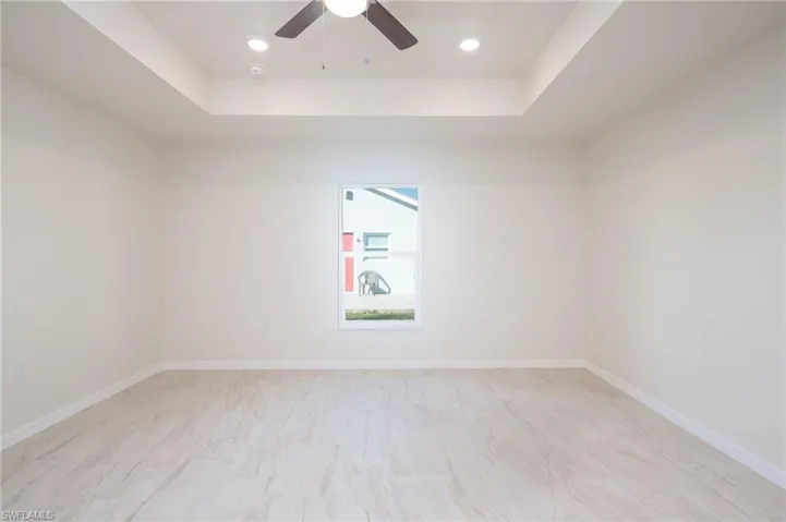 Empty room with ceiling fan and a tray ceiling