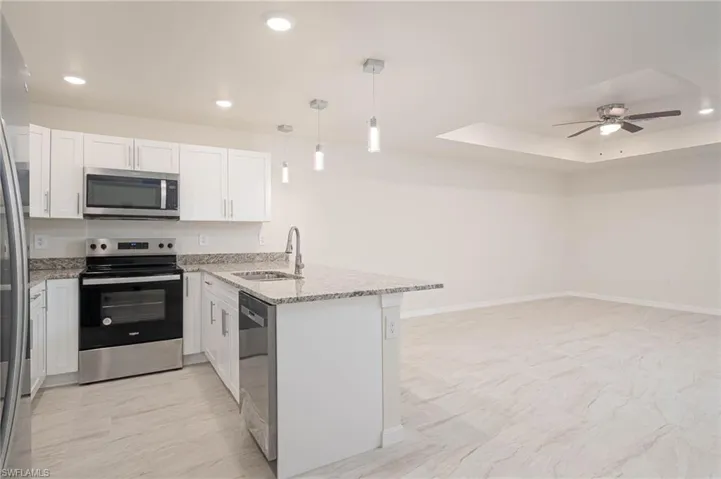 Kitchen featuring appliances with stainless steel finishes, decorative light fixtures, sink, white cabinets, and kitchen peninsula