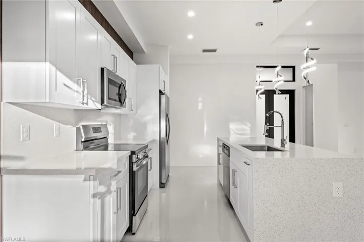Kitchen with stainless steel appliances, light stone counters, decorative light fixtures, white cabinets, and a center island with sink