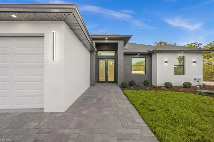 View of exterior entry with stucco siding, a lawn, a garage, roof with shingles, and french doors
