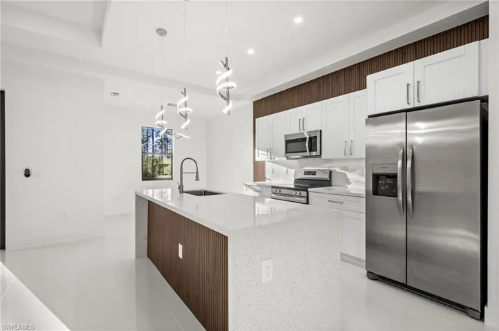 Kitchen featuring stainless steel appliances, white cabinetry, decorative light fixtures, light stone countertops, and an island with sink