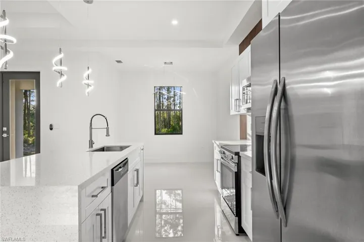 Kitchen with stainless steel appliances, white cabinets, pendant lighting, light stone counters, and a center island with sink