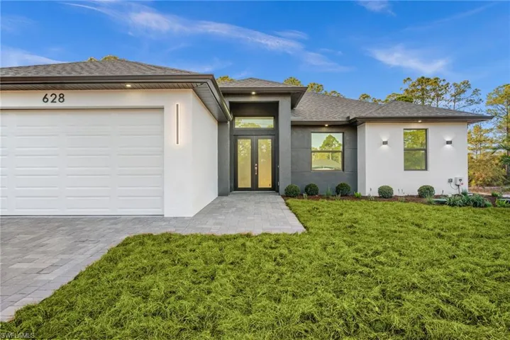 View of front of house with french doors, stucco siding, a front lawn, decorative driveway, and a shingled roof