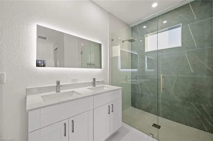 Bathroom featuring a textured wall, double vanity, a marble finish shower, and recessed lighting