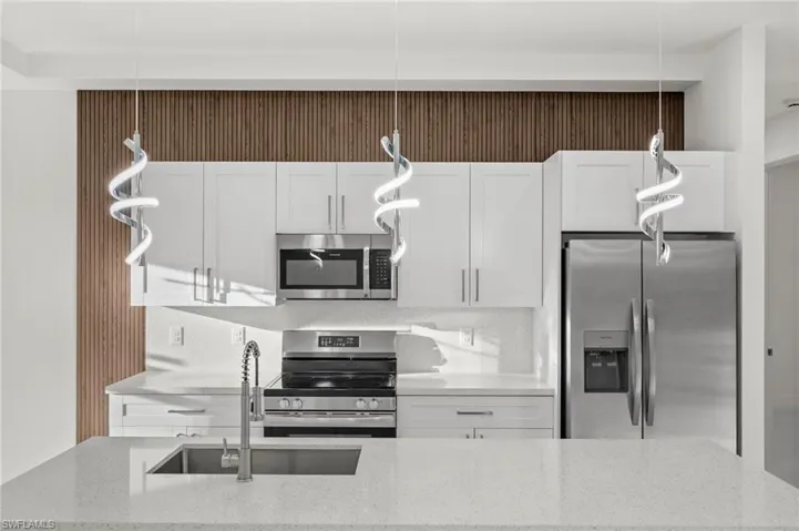 Kitchen with stainless steel appliances, decorative light fixtures, light stone counters, and white cabinetry