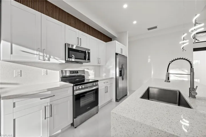 Kitchen featuring stainless steel appliances, light stone countertops, and white cabinetry