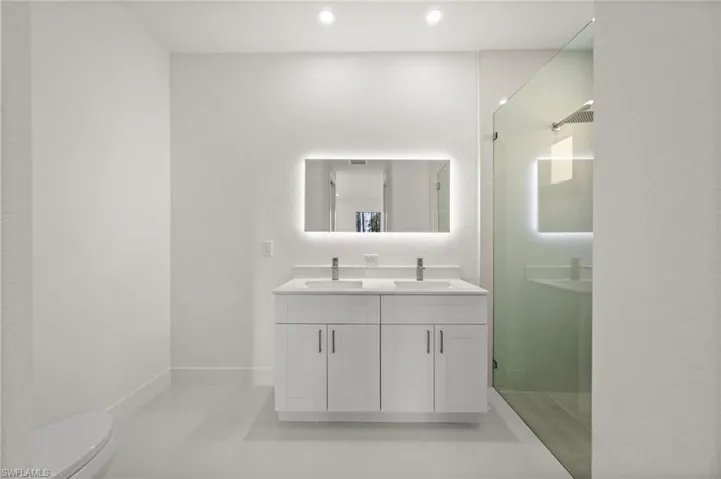 Full bathroom featuring double vanity, a shower stall, a textured wall, and recessed lighting