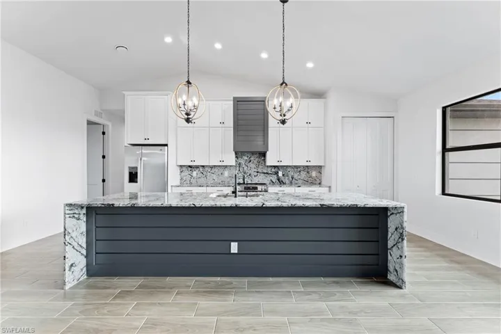 Kitchen with light stone countertops, white cabinetry, stainless steel refrigerator with ice dispenser, a spacious island, and lofted ceiling