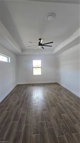 Empty room with a ceiling fan, wood finish floors, and a tray ceiling