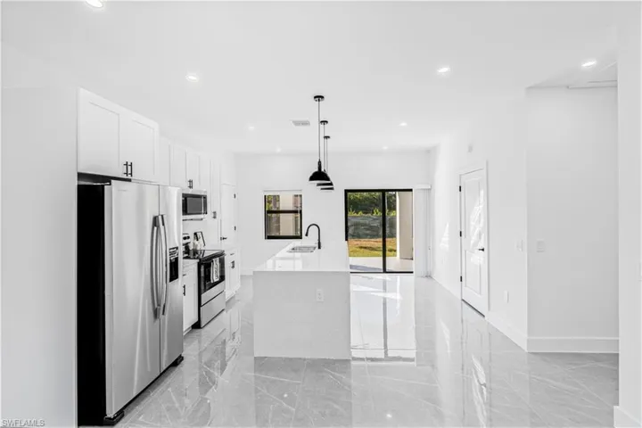 Kitchen featuring stainless steel appliances, a kitchen island with sink, white cabinetry, light stone counters, and pendant lighting