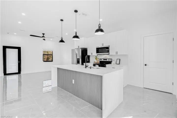 Kitchen featuring an island with sink, white cabinetry, stainless steel appliances, light stone counters, and pendant lighting