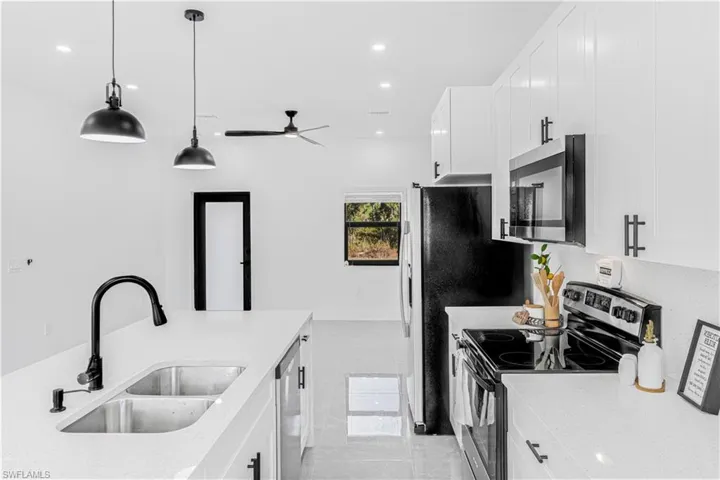 Kitchen with stainless steel appliances, light stone countertops, hanging light fixtures, white cabinets, and ceiling fan