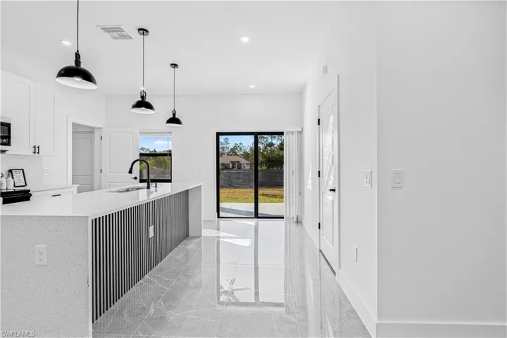 Kitchen featuring light stone countertops, white cabinets, decorative light fixtures, an island with sink, and light marble finish floors
