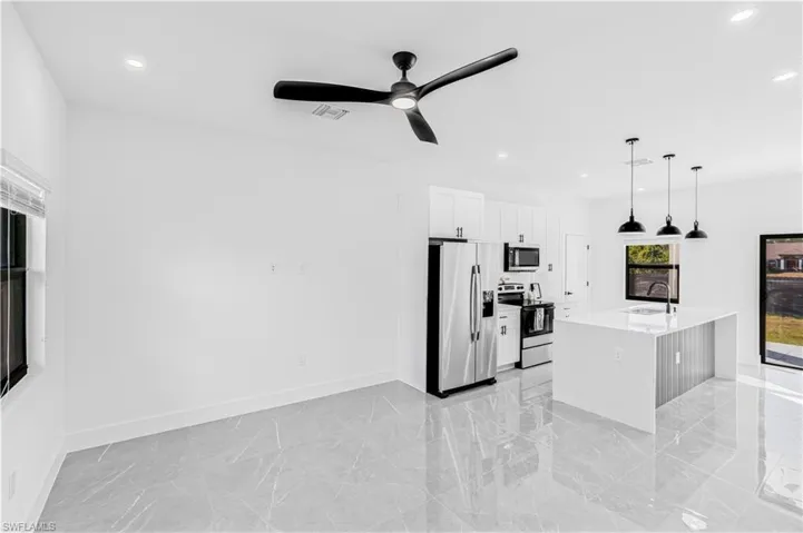 Kitchen with stainless steel appliances, light stone countertops, an island with sink, white cabinets, and ceiling fan